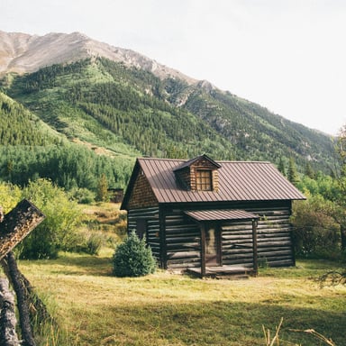 Rustic log cabin in a Colorado mountain valley with green hillsides