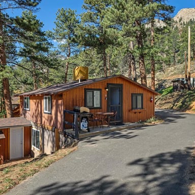 Cedar cabin exterior with patio seating tucked among pines and granite rocks in Estes Park