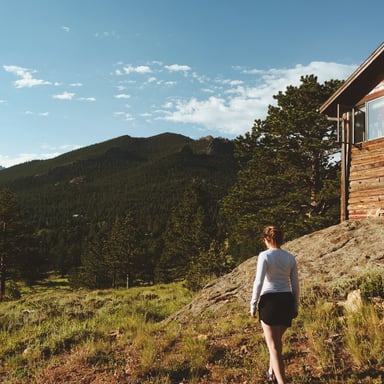 Person walking toward a log cabin with Colorado mountain views